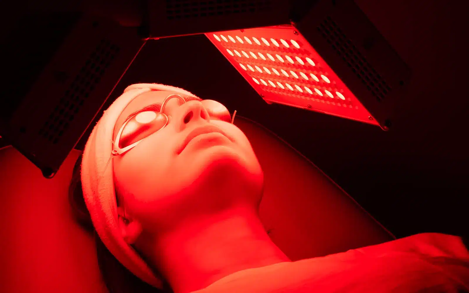Personne portant des lunettes et un bandeau, sous lumière rouge intense d’un appareil de photothérapie LED.